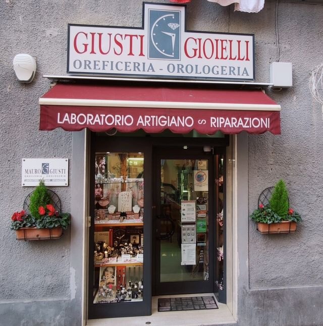 L’ingresso del negozio: l’insegna Giusti Gioielli, Oreficeria - Orologeria, e la tenda rossa con la scritta Laboratorio artigiano, riparazioni